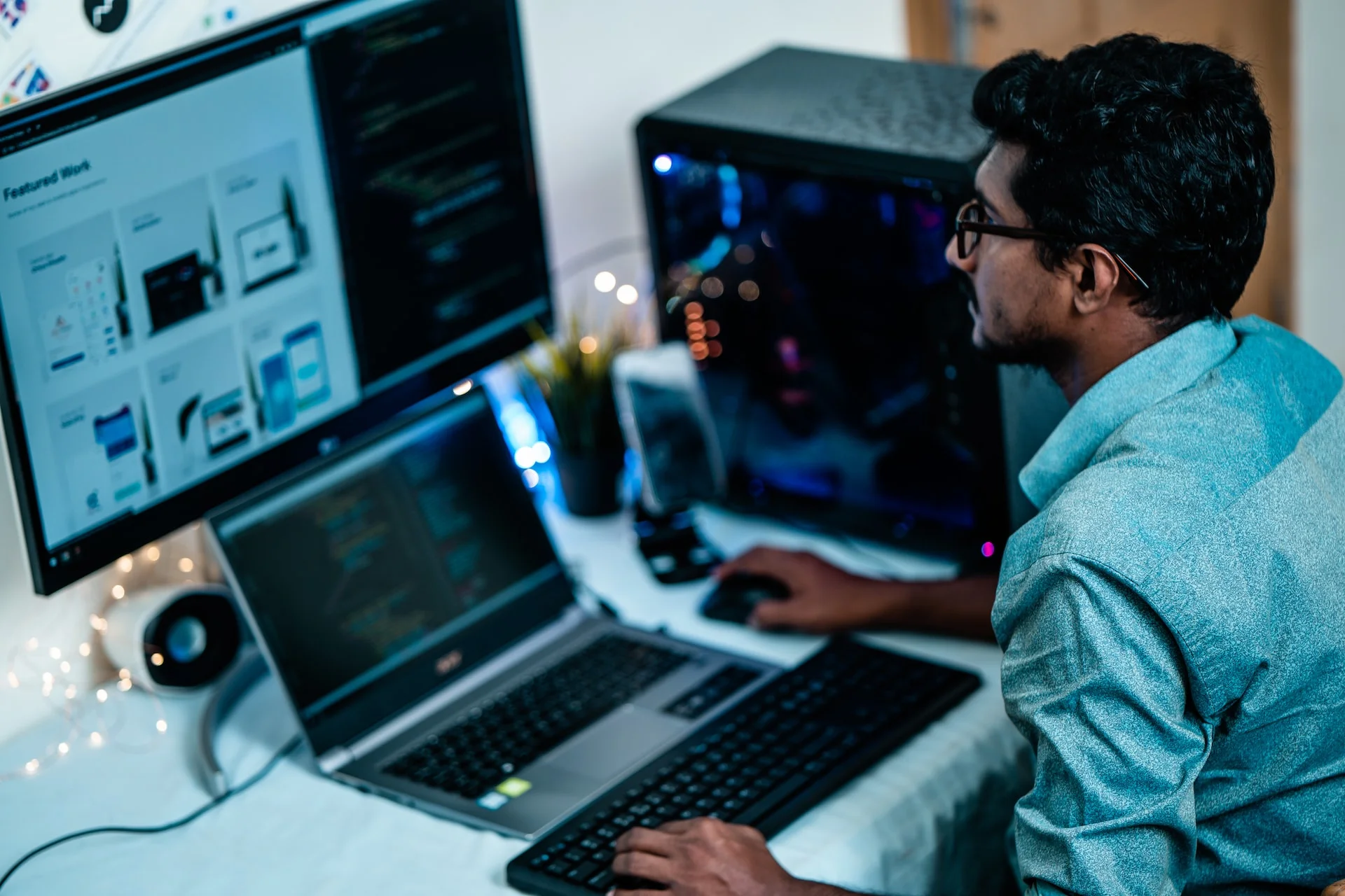 A man at a work station in front of a laptop and a desktop computer