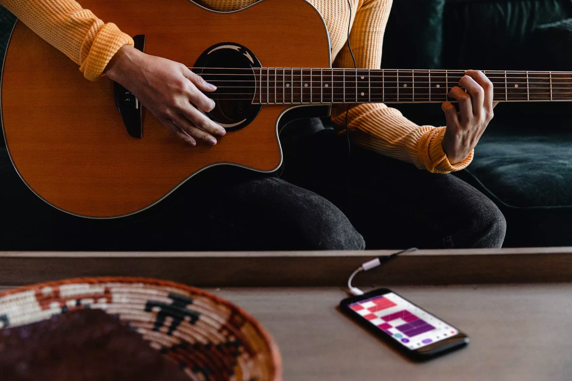 Phone connected to a guitar being played by a person.