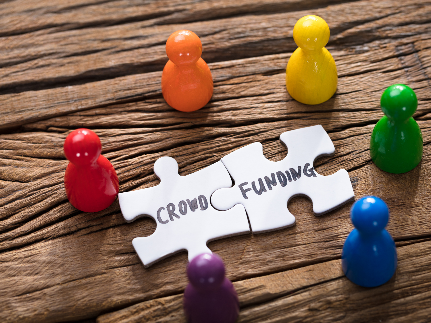 five figurings on the table placed around two pieces of a puzzle that have the words "crowd funding"