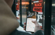 A person using a smartphone to check a store’s information, payment methods, and customer reviews in front of a Black Friday sale display.