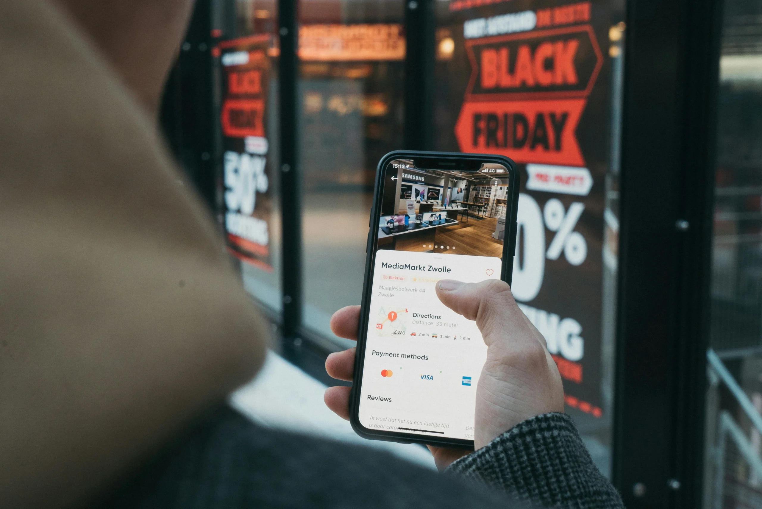 A person using a smartphone to check a store’s information, payment methods, and customer reviews in front of a Black Friday sale display.